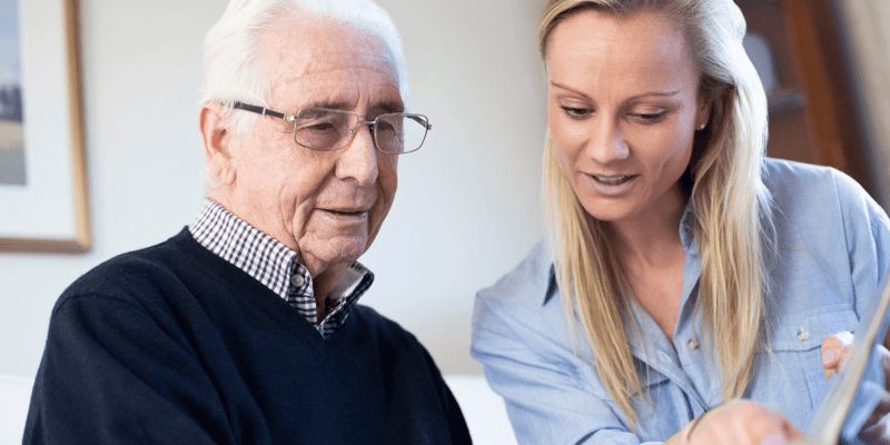 An older man looking at a photo album with his adult granddaughter